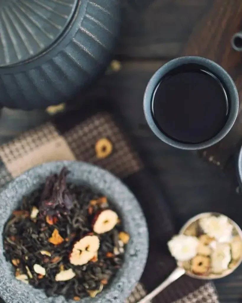 Teapots, cups of tea and a bowl of loose tea on a dark wooden table, seen from above