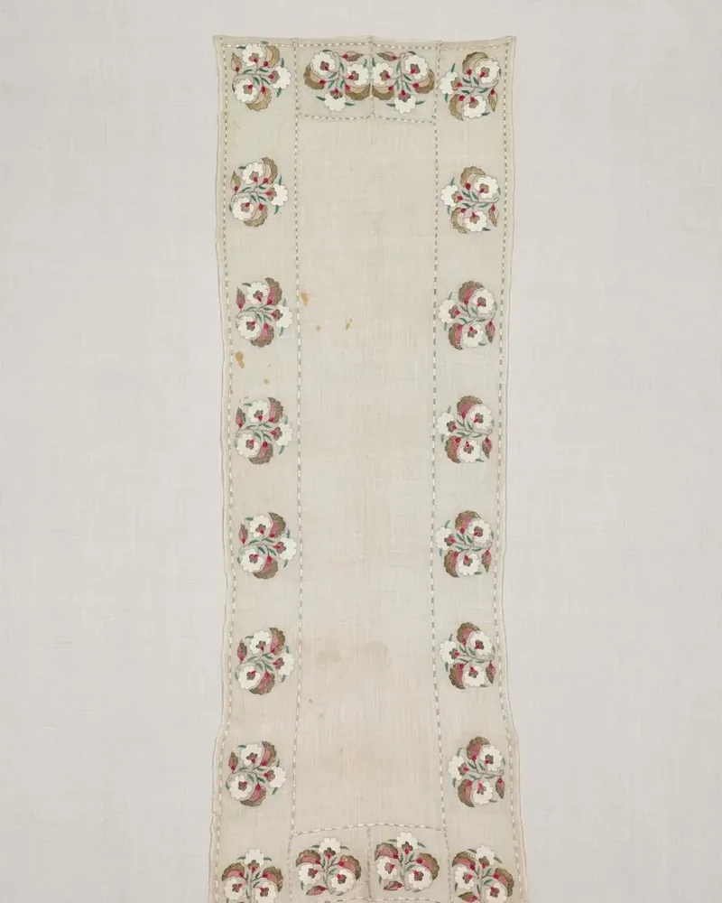 A long cream linen table runner with embroidered floral motifs along its edges