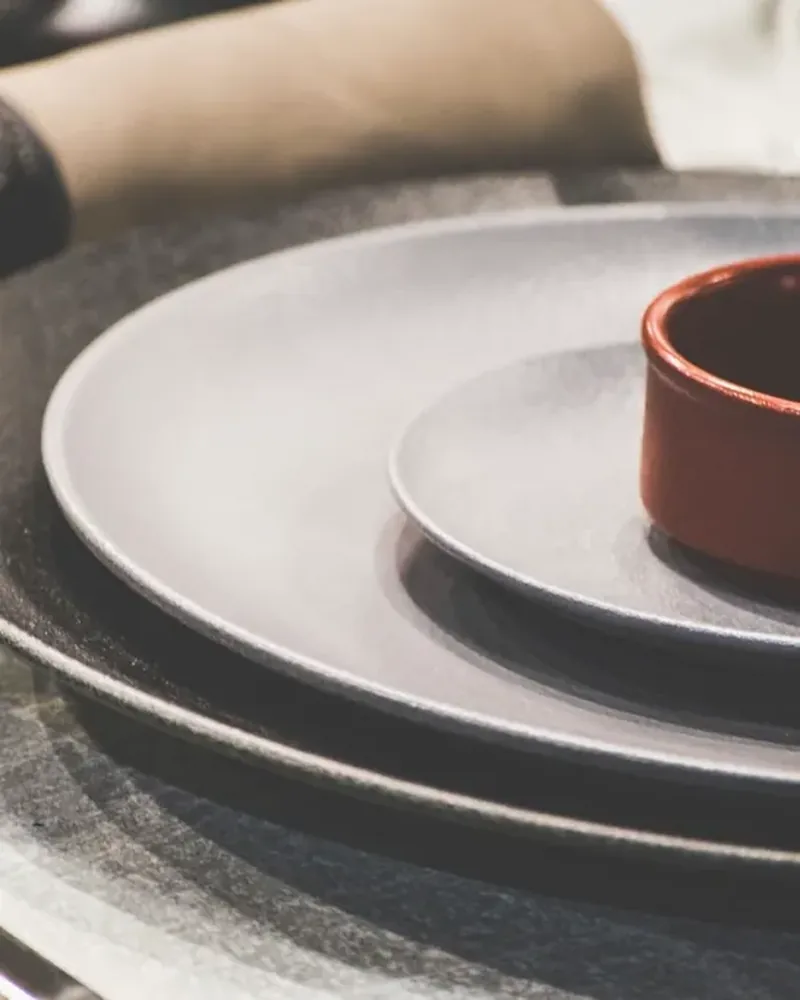 Stacked grey stoneware plates with a small red bowl and a fork on a table