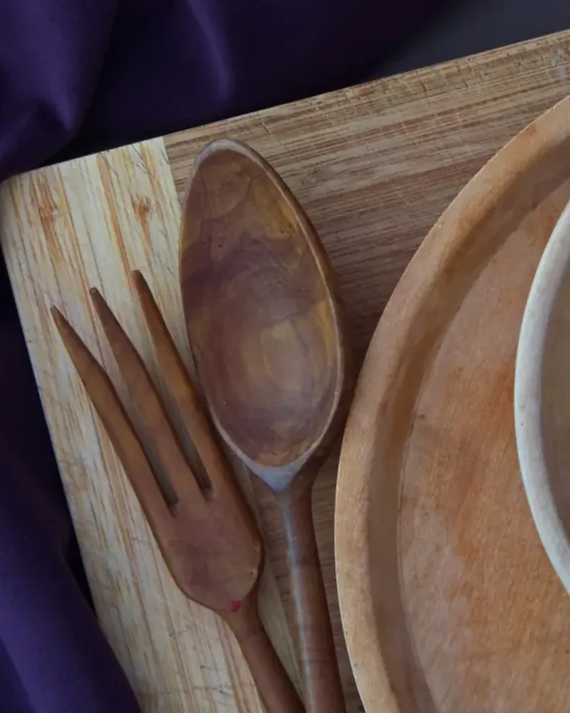 A wooden serving board with a turned wooden plate, fork and spoon, seen from above