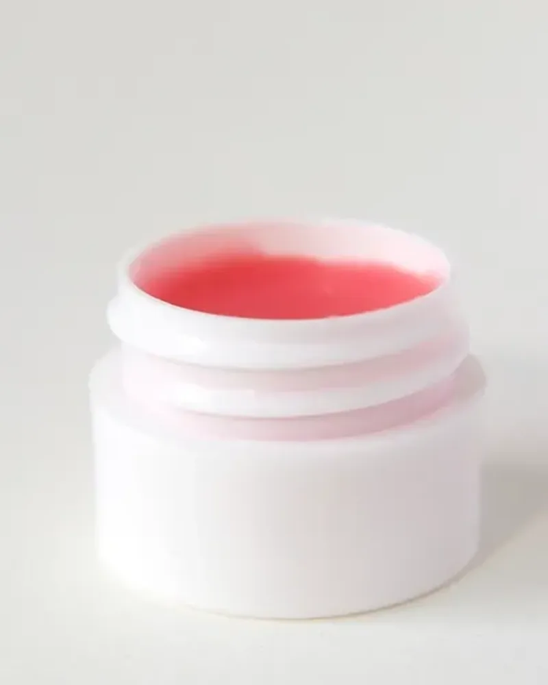 A small white cosmetic jar with a pink balm, on a pale grey background