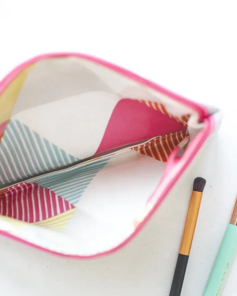 An open fabric cosmetics pouch with two makeup brushes on a white surface