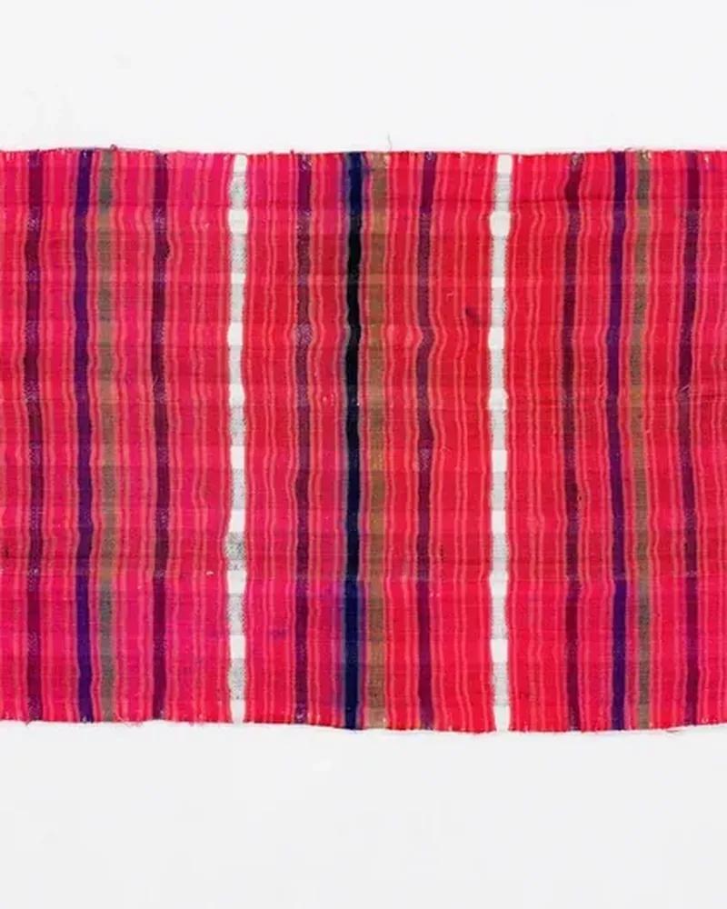 A handwoven striped scarf in pink, red and white, laid flat on a white background