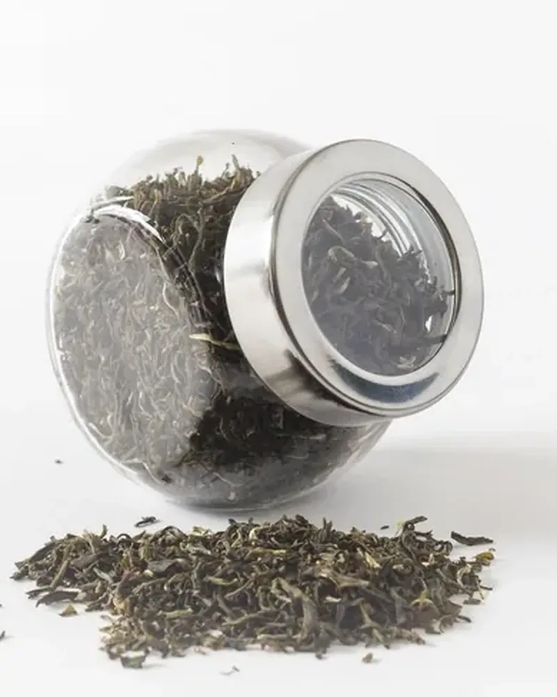 A glass jar of loose black tea leaves with a small heap of leaves in front
