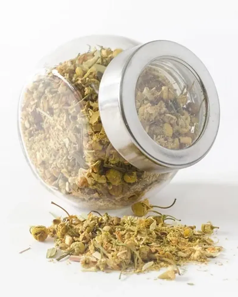 A glass jar of a yellow dried herbal blend with a small heap in front