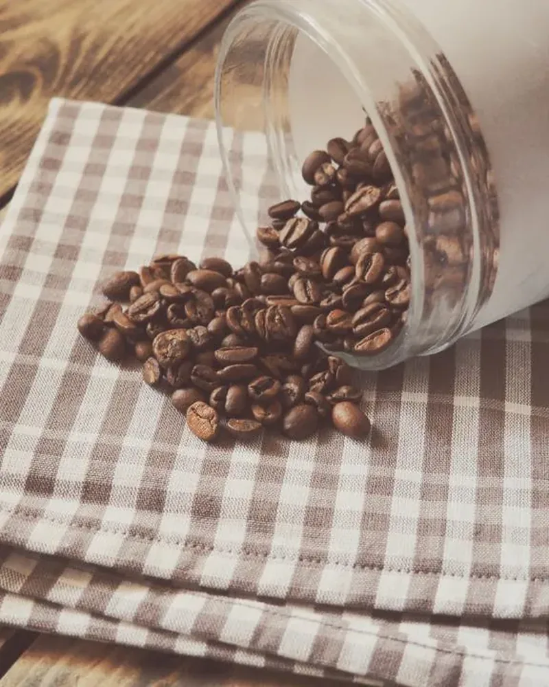 Roasted coffee beans spilling from a glass jar onto a checked cloth