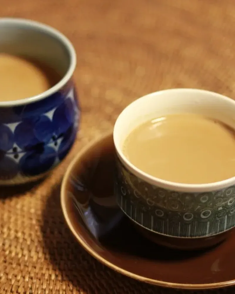 Two cups of milky masala chai on a rattan tray