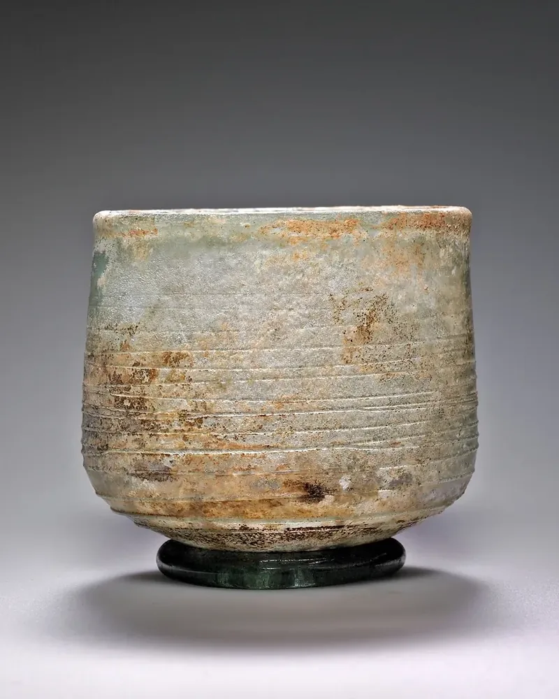 A rustic handleless ceramic tea cup with a textured glaze on a grey background