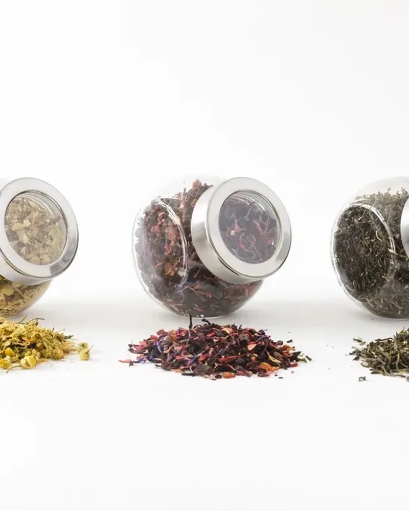 Three glass jars of different loose teas, each with a small heap of leaves in front