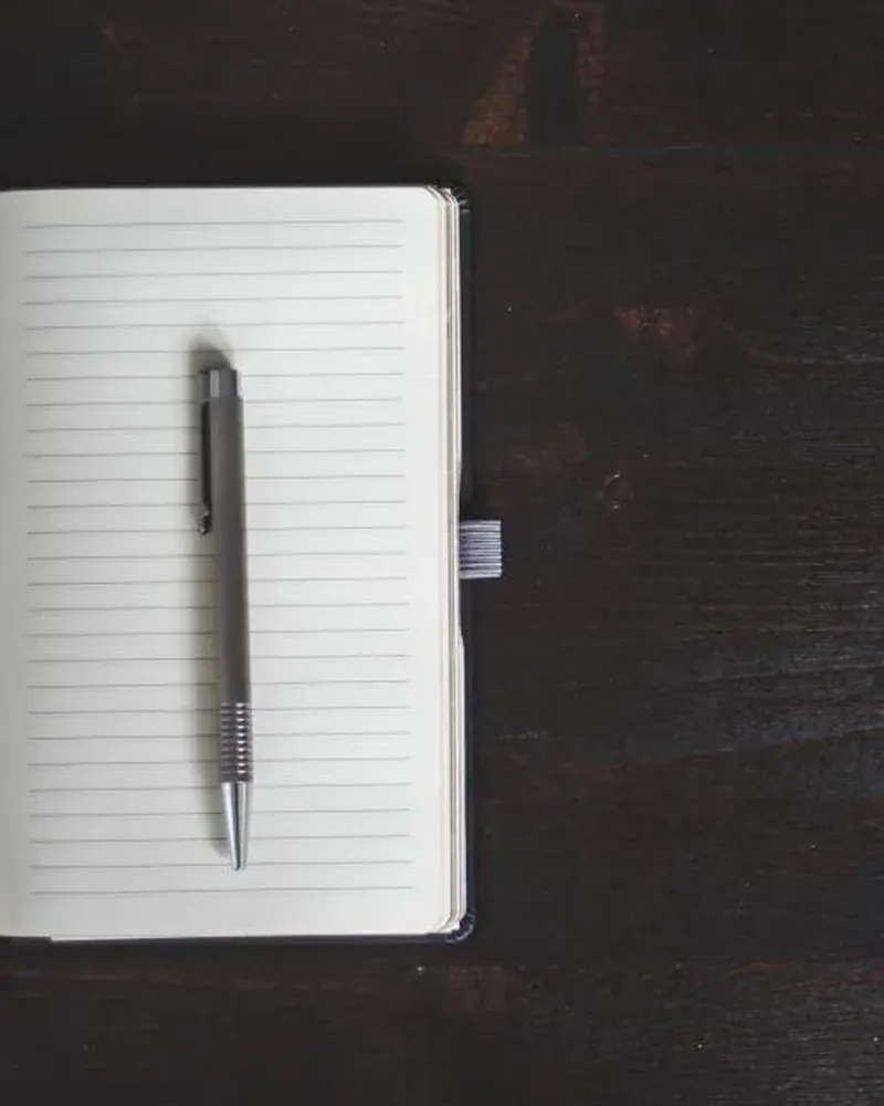 A closed notebook with an elastic band and a pen on a dark wooden table
