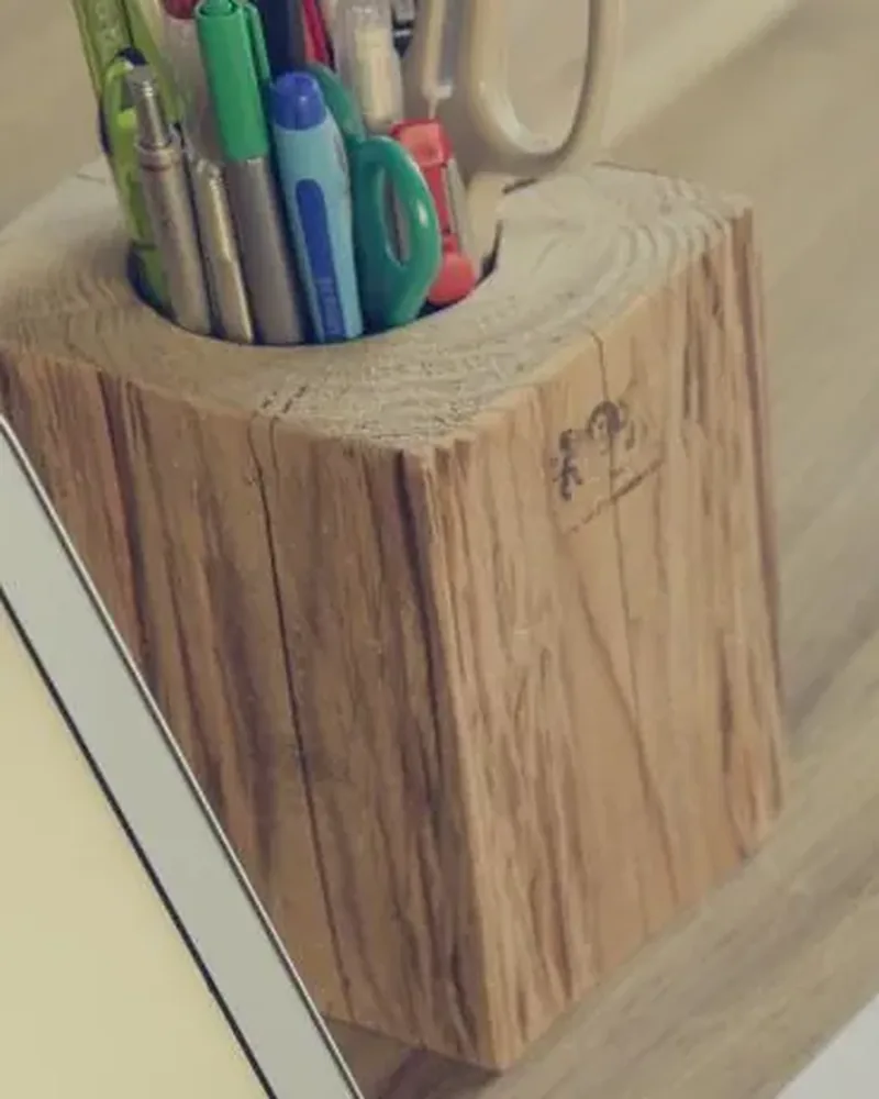 A square wooden pen holder filled with coloured pencils on a wooden desk