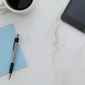 A light blue notepad and a pen on a white marble desk