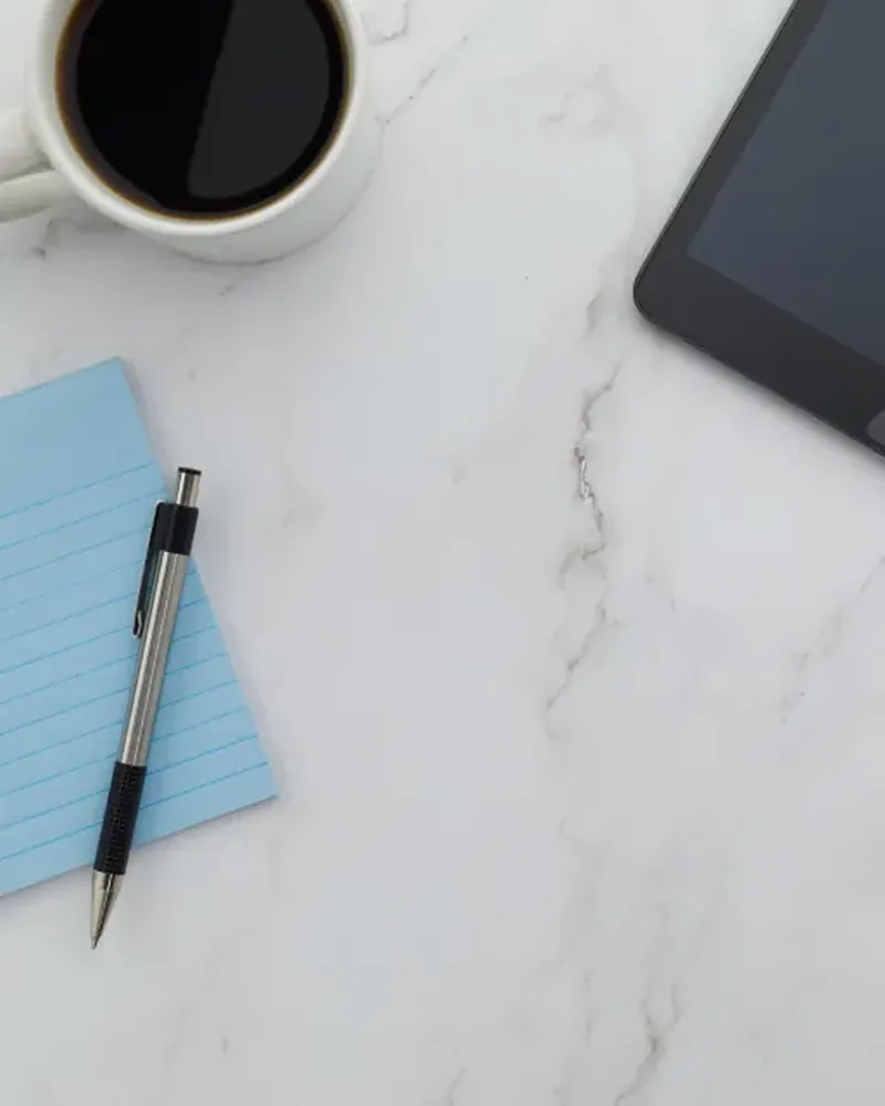 A light blue notepad and a pen on a white marble desk